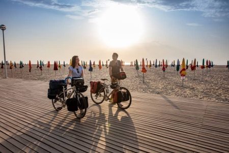 image de deux cyclistes sur la plage ensoleillée de deauville avec plein de parasoles fermés